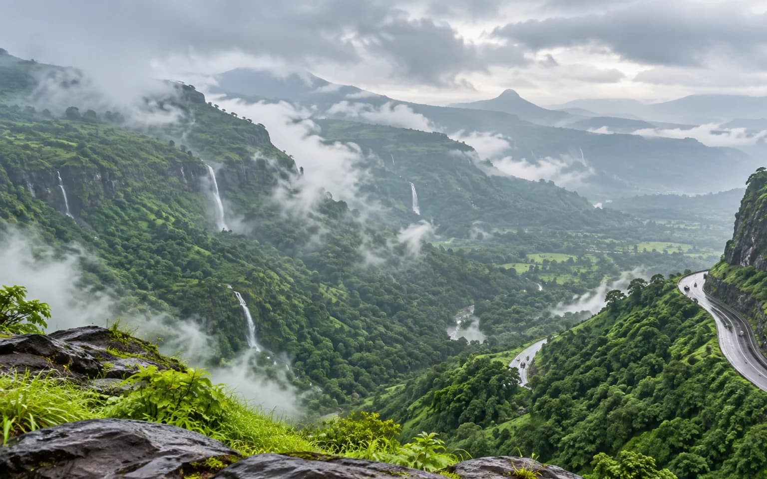 Cloud-wrapped green ridges and winding mountain road near Khandala